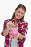 Portrait of a young woman putting a note a piggy bank