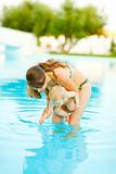 Mother showing water to baby standing in swimming pool