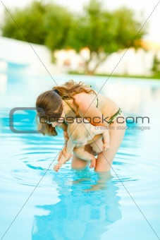 Mother showing water to baby standing in swimming pool