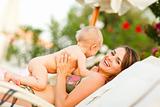 Smiling young mother with baby relaxing on sunbed