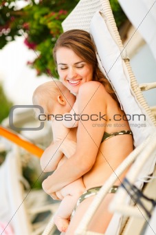 Happy young mother laying on sunbed and hugging baby