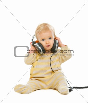 Cute baby in headphones sitting on floor isolated on white