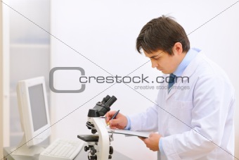 Researcher using microscope in medical laboratory and taking notes