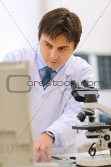 Researcher working in medical laboratory using microscope and computer