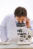 Researcher looking in microscope and speaking mobile in medical laboratory