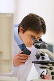Researcher looking in microscope and making notes on voice recorder in laboratory