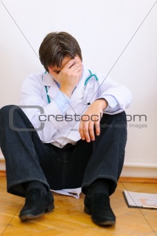 Upset medical doctor sitting on floor