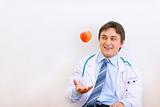 Smiling medical doctor sitting on floor and throwing up apple