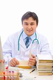 Smiling medical doctor sitting at table and reading book