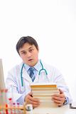 Stressed medical doctor sitting at table with stack of books