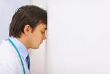 Tired medical doctor leaned his head into a wall