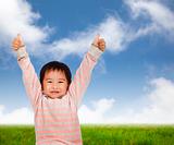 Smiling kid with thumbs up and standing on the green meadow