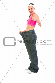 Slim girl pulling oversize jeans and showing thumbs up. Weight loss concept