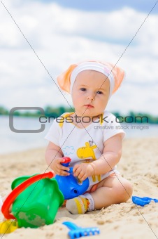cute baby girl playing on the beach with sand.