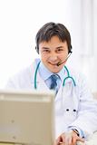 Smiling medical doctor with headset working on pc