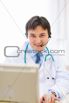 Smiling medical doctor with headset working on pc