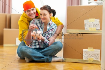 Young couple among boxes putting coin in piggy bank