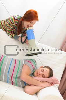 Red hair girl shouting through megaphone to sleeping boyfriend