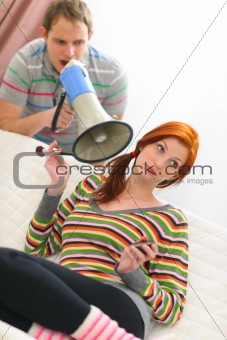 Young man shouting through megaphone to too long applying makeup girlfriend