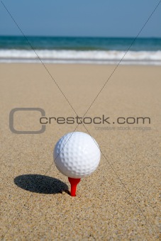 A golf ball on the beach, ready to be hit in to the ocean.