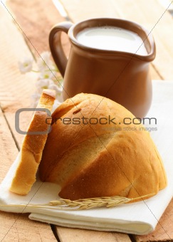 Ceramic jug with milk and a loaf of bread on a wooden table , rustic style