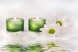 Green candles and daisies near water reflection