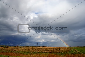 Clouds and rainbow above meadow