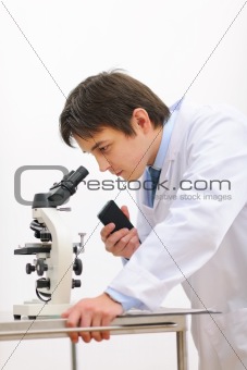Researcher looking in microscope and making notes on voice recorder