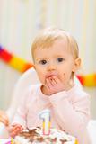 Portrait of eat smeared baby eating first birthday cake