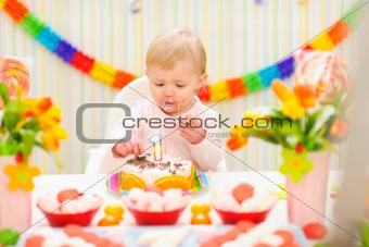 Portrait of eat smeared baby eating birthday cake