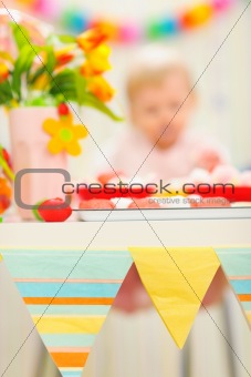 Closeup on table decorated for birthday celebration and baby in background|anonymous