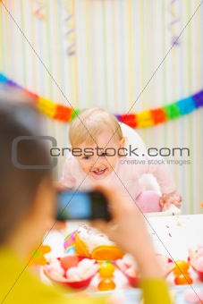 Mother making photos of happy baby on first birthday party