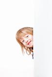 curious boy with long blond hair peeking out from behind a white board looking
