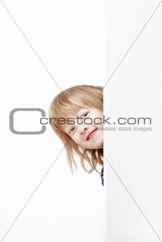 curious boy with long blond hair peeking out from behind a white board looking