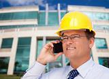 Handsome Contractor in Hardhat and Necktie Smiles as He Talks on His Cell Phone in Front of Building.
