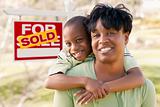 Happy African American Mother and Child In Front of Sold Real Estate Sign.