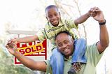 Happy African American Father and Son in Front of Sold Real Estate Sign.