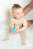Cute baby held by father's hands, playing with rubber toy and smiling while taking a bath