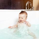Cute baby having fun, splashing water and laughing while taking a bath in a modern bathroom interior
