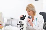 Senior doctor woman looking in microscope and making voice notes