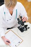 Closeup on researcher working with microscope and making notes in clipboard