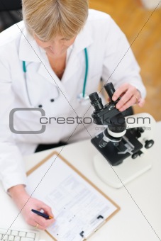 Closeup on researcher working with microscope and making notes in clipboard