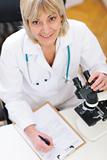 Senior researcher woman working with microscope and making notes in clipboard