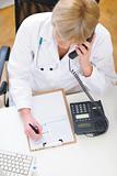 Doctor woman speaking phone and making notes in clipboard