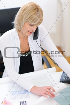 Senior architect woman speaking phone and looking on blueprints