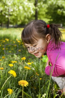  A smiling girl wearing a pink shirt, sitting on the dandelion f
