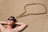 smiling young man lying on the beach and dialog symbol