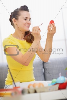 Smiling woman painting on red Easter egg