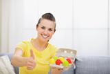 Smiling woman holding tray with colorful Easter eggs and showing thumbs up