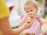 Mother giving baby cookie in shape of Easter egg. Focus on cookie